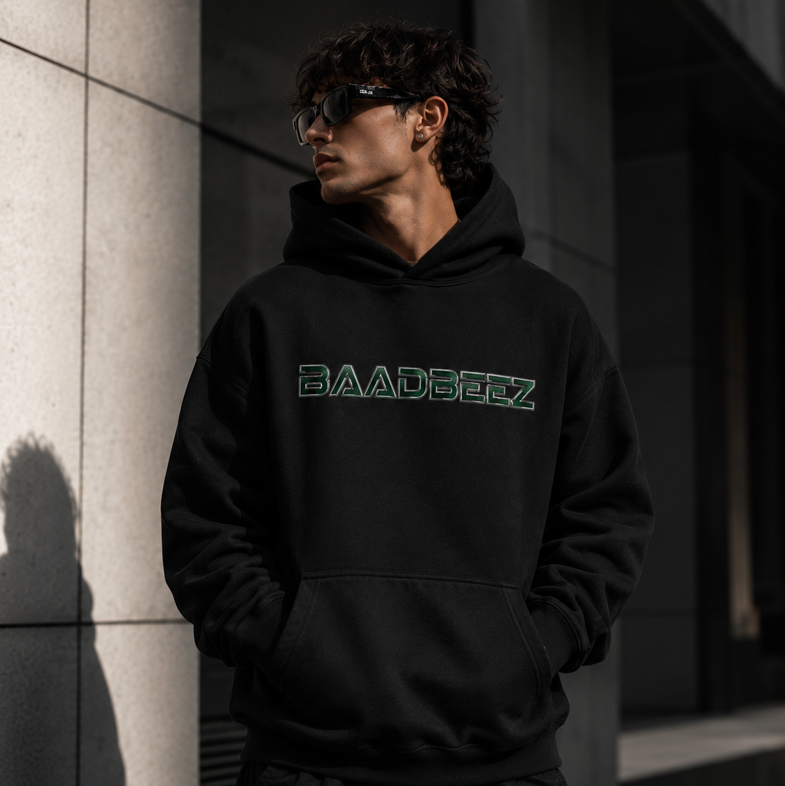 Person wearing a black hoodie with 'BAADBEEZ' logo against a dark background